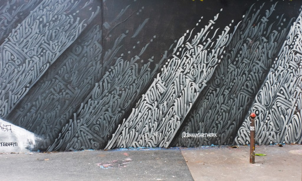 artwork by Johnny Ashbaugh on a Paris wall, diagonal sections of calligraphy in black, grey, and white 