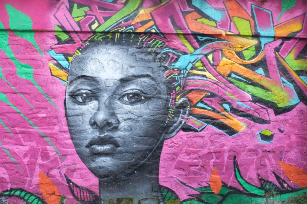 mural on bright pink background, portrait of a black woman with long pink, orange, and green hair