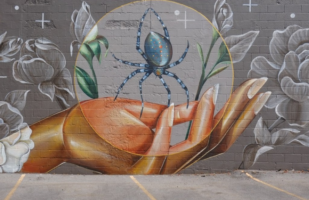 Close up of blue spider on woman's hand, very long fingernails.   Spider is blue with striped legs and small red and white dots on its back 
