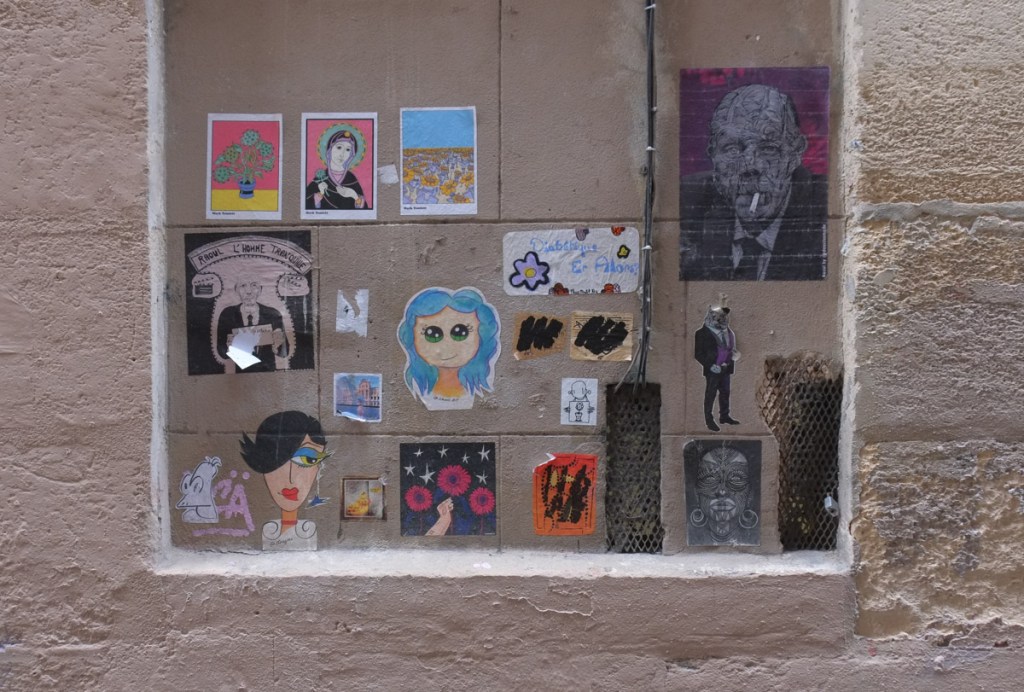 wall with a collection of graffiti wheatpasted onto to it, small paper graffiti