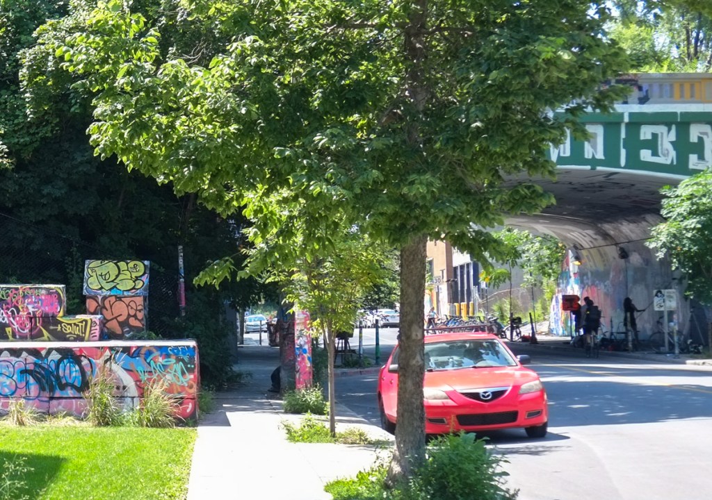 looking down rue Rouen in Montreal towards railway bridge, people painting the walls under the bridge