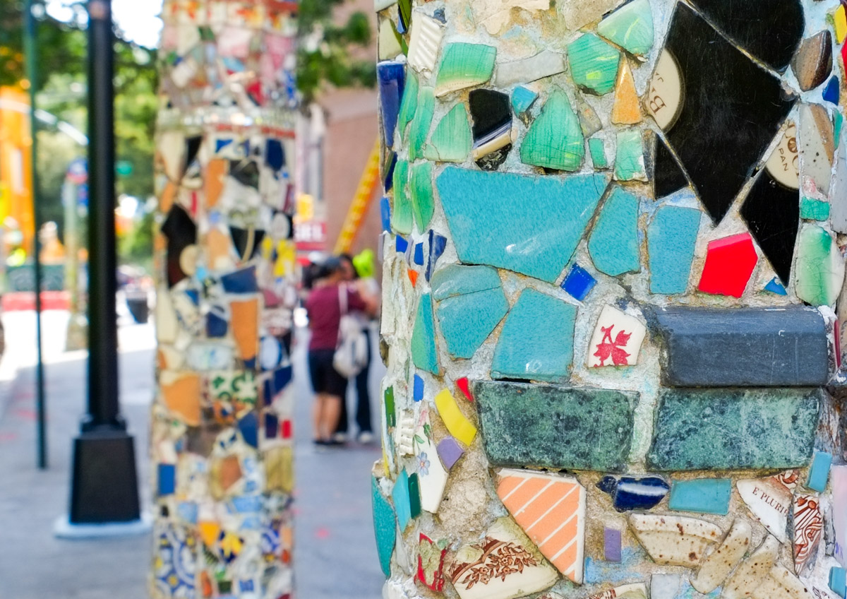 mosaics on two lamp posts, one closer and in focus, the other in the background, some people standing on the sidewalk too