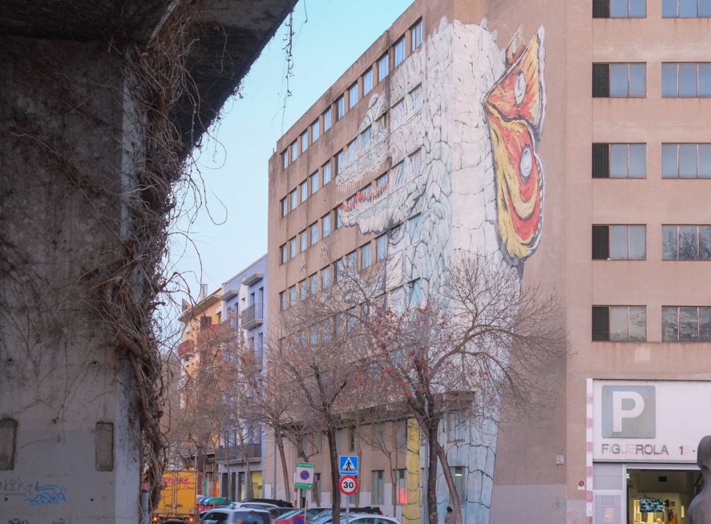 mural of a large crocodile with butterfly wings on its back, standing on its hind legs, reaching for flying insects to eat, on the side of an apartment building