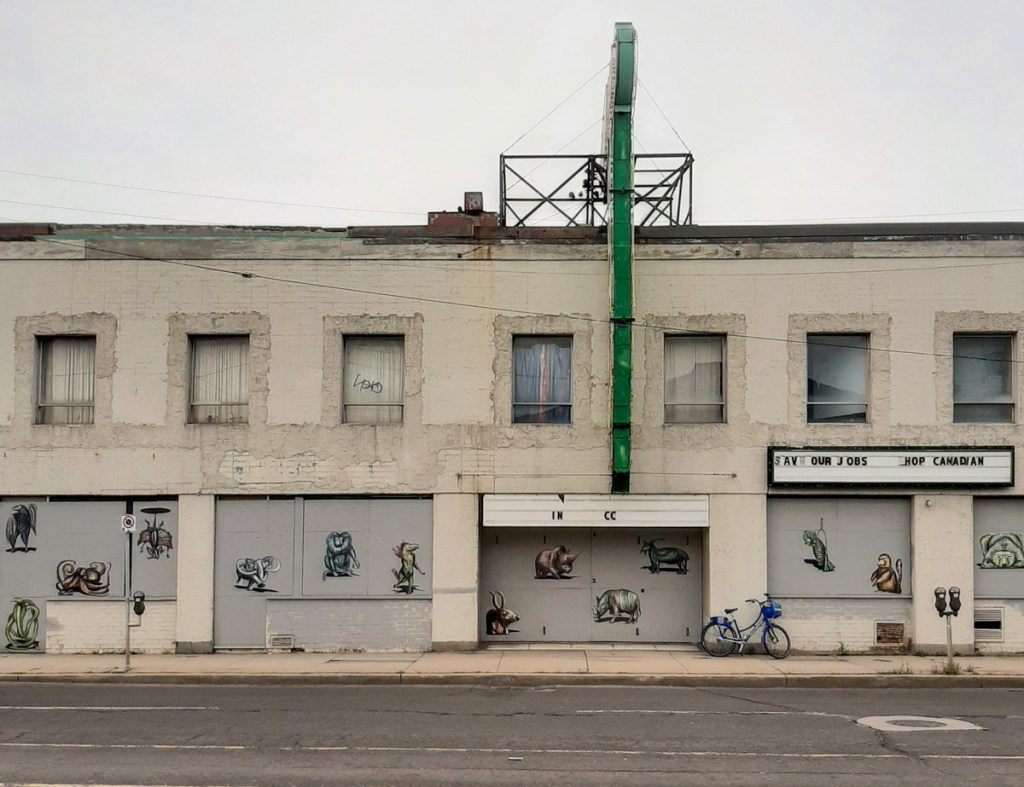 front of an empty and boarded up grey two storey building in downtown Hamilton that now has many wheat paste images of animals 