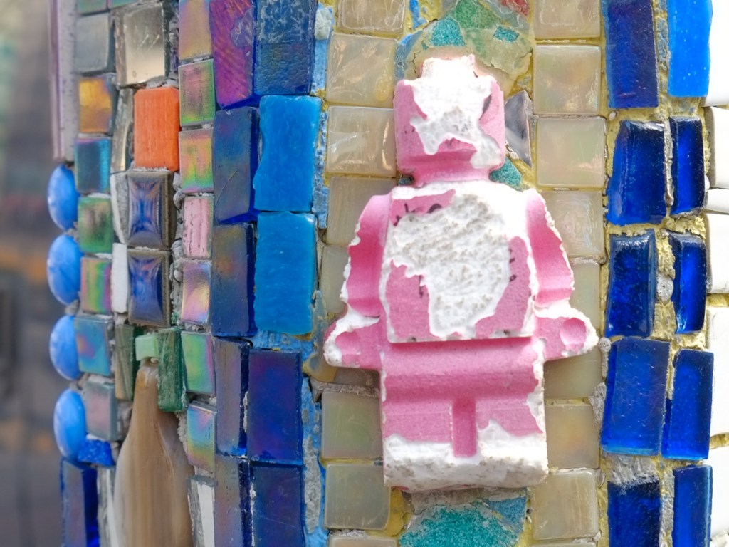 mosaics on a pole, glass beads, squares, pink coloured lego figure that has been damaged,
