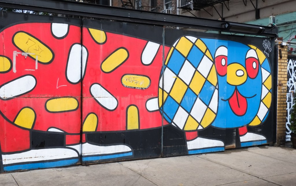 large mural of a stylized dog with red body and blue head, and big white floppy ears with yellow and blue diamond shapes, yellow and white spots all over body, red tongue sticking out, yellow button nose