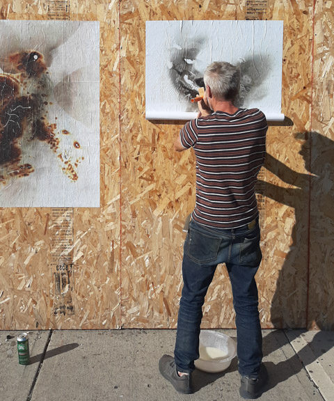 shadow play, while pasting firegrams by Danielle Goshay on the exterior of an abandoned and boarded up building