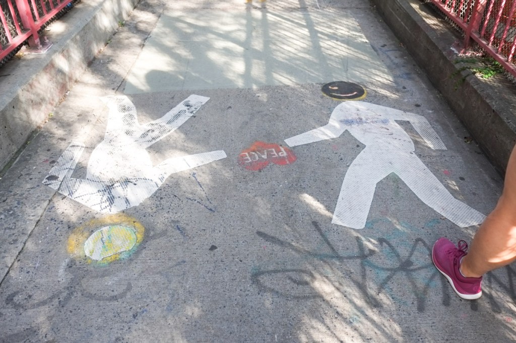 graffiti on the sidewalk, two white people, one with sign reaching out for the other