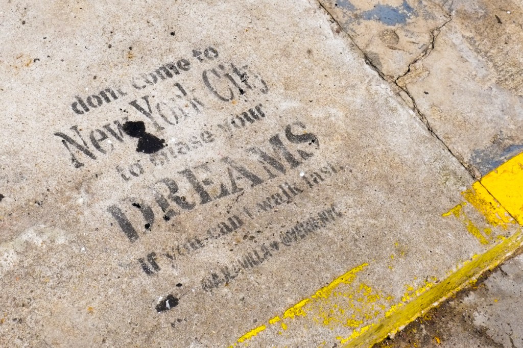 text graffiti on a concrete sidewalk that says Don't come to New York City to chase your DREAMS If you can't walk fast