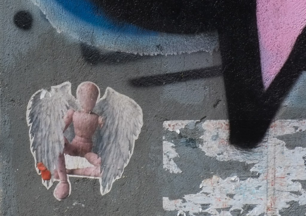 graffiti featuring little wood mannequin on one knee, with white feathered angel wings