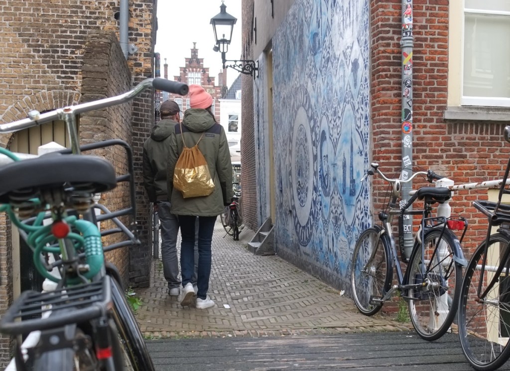 couple walking past parked bikes to small alley with a blue and white mural, bonte ossteeg