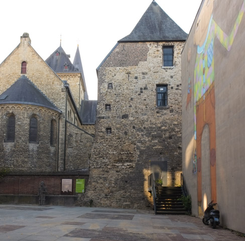 back of very old stone church, black late roofs, mural on wall beside