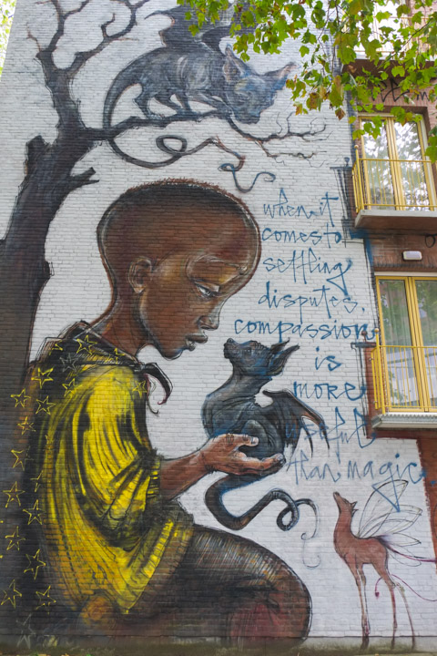 a young black boy kneels under a tree with a small dragon in his hands.  a second dragon sits on a branch of the tree and is looking down.  Text in the mural says When it comes to settling disputes, compassion is more useful than magic