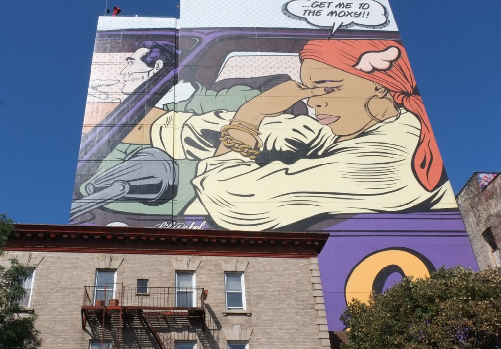 mural by d face on upper storey of moxy hotel in williamsburg, a woman passenger in a car, man driving, woman is thinking, just get me to the moxy