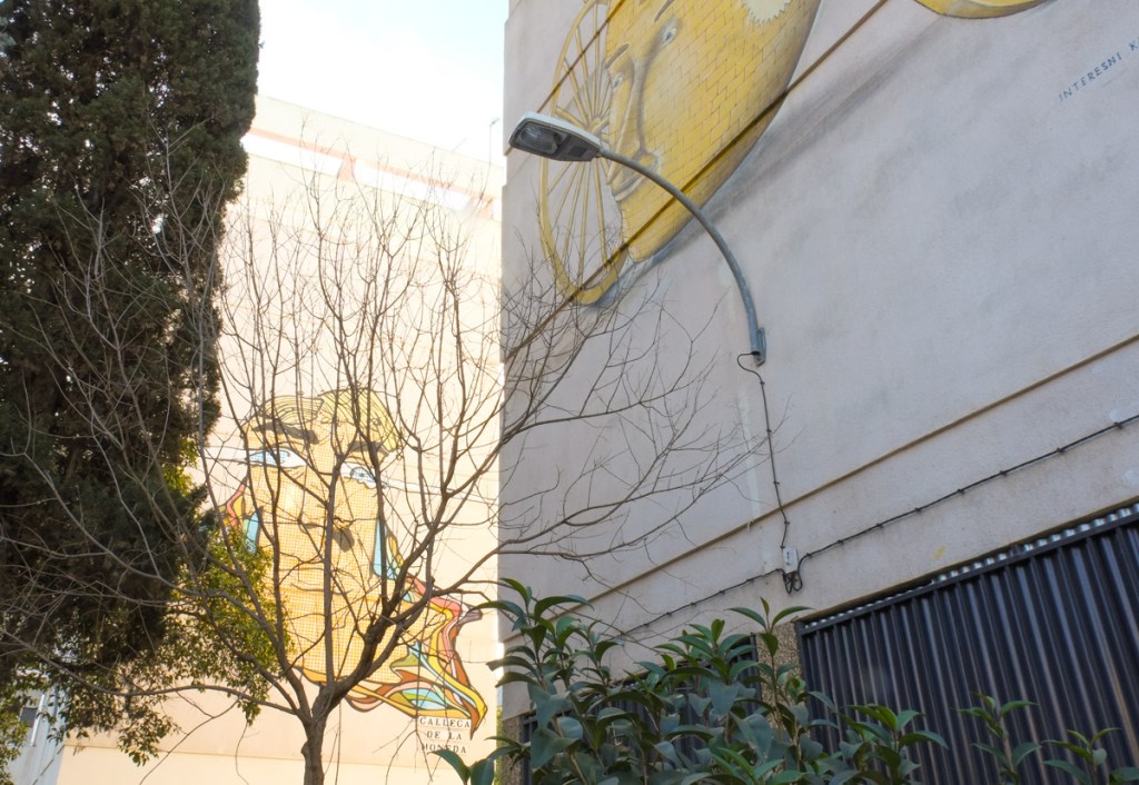 part of 2 murals on 2 adjacent buildings, one is a portrait of a man with a large tree in front of it