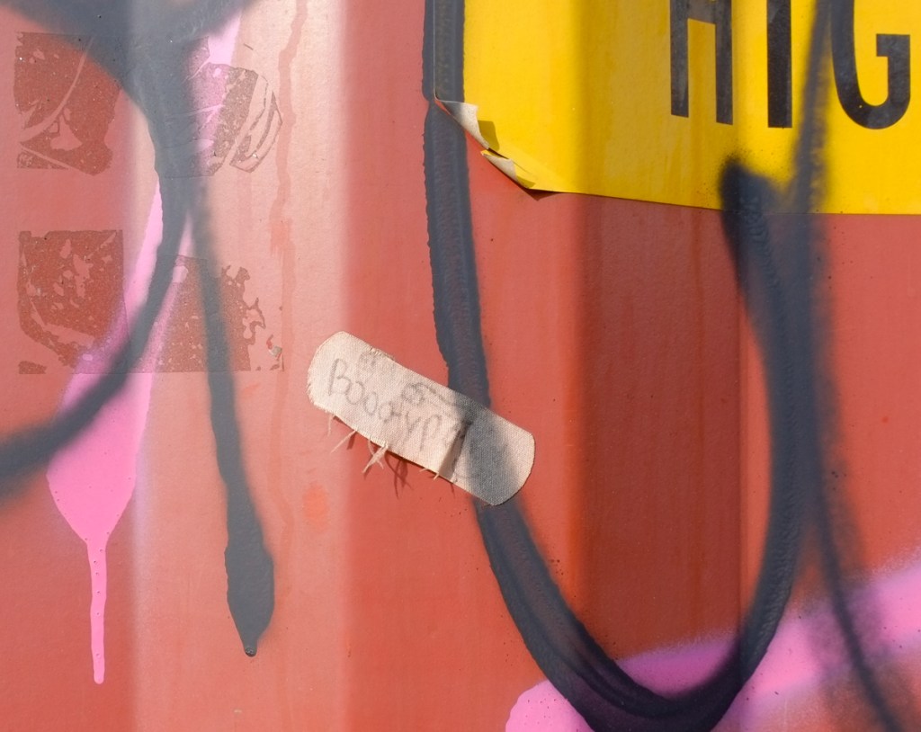 close up of drips of paint and other spray paint graffiti, an old band-aid with pen written words in it is stuck to the wall