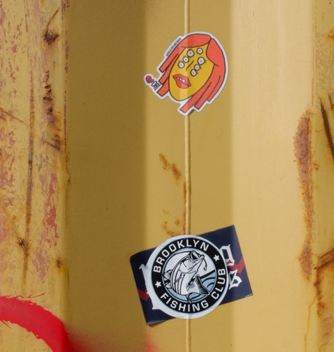 two graffiti stickers, one is brooklyn fishing club and the other is a sold out art sales face with three sets of eyes 
