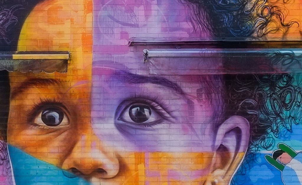 close up of child's eyes in a large mural, painted by Joel Artista in 2019, in oranges and purples