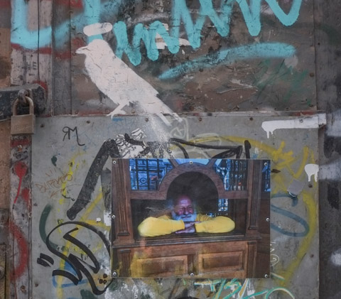 a photo of a man looking out a window, pasted on exterior wall, with painting of a white raven sitting on top of the photo