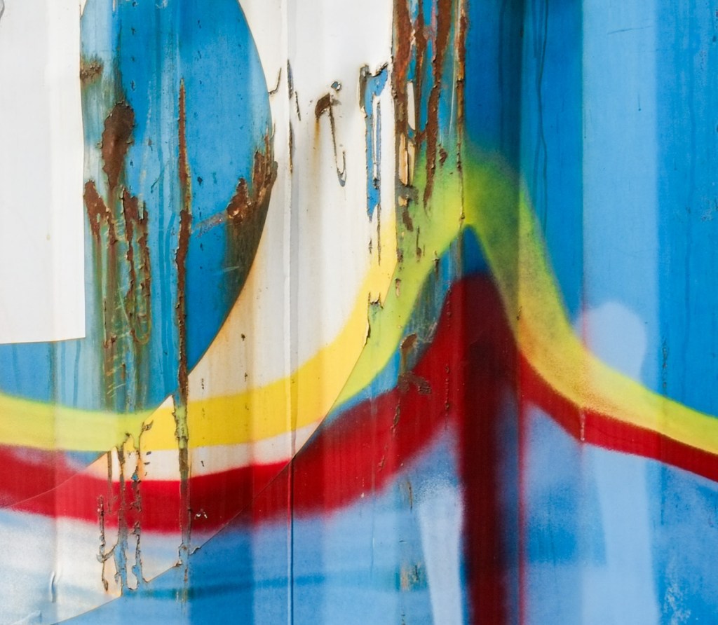 small section of graffiti, curved lines in white, yellow, and red, on blue background, with some rust from the metal container showing through