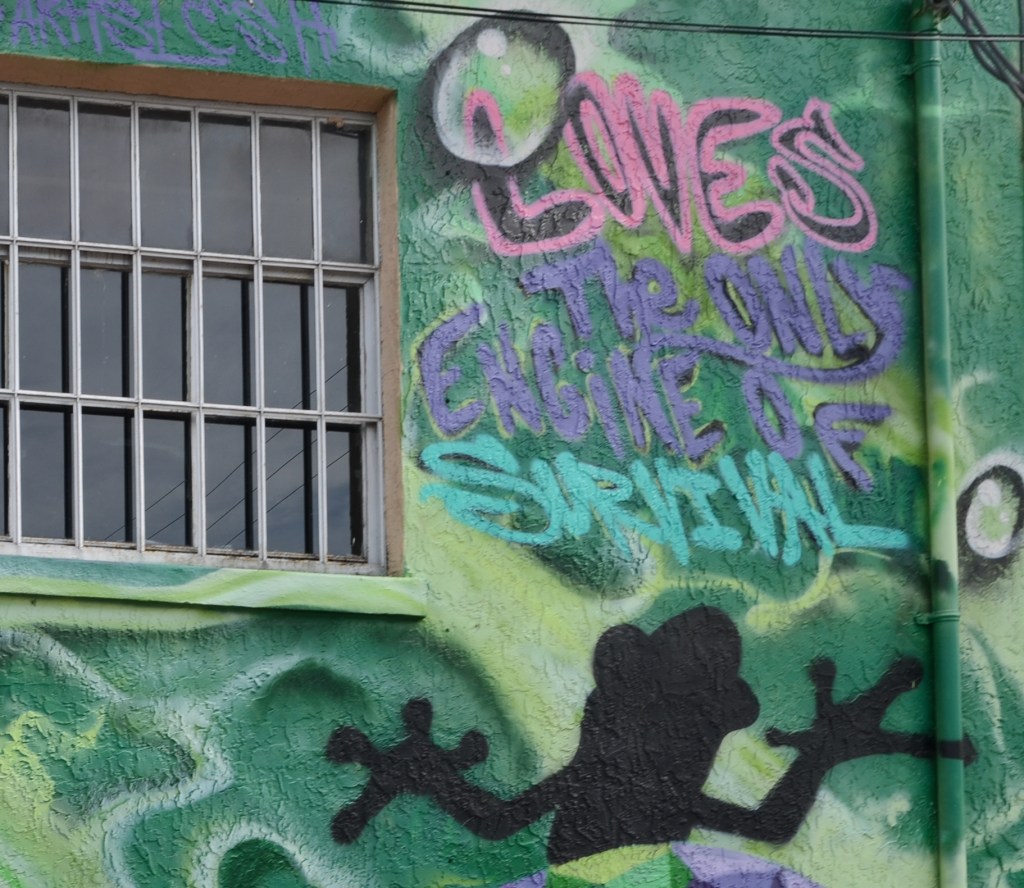 words painted on a wall in the corner of a green mural that says love's the only engine of survival
