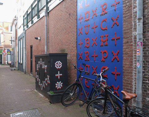 looking down an alley in delft, bikes leaning against wall on right along with a large panel painted blue with red letters