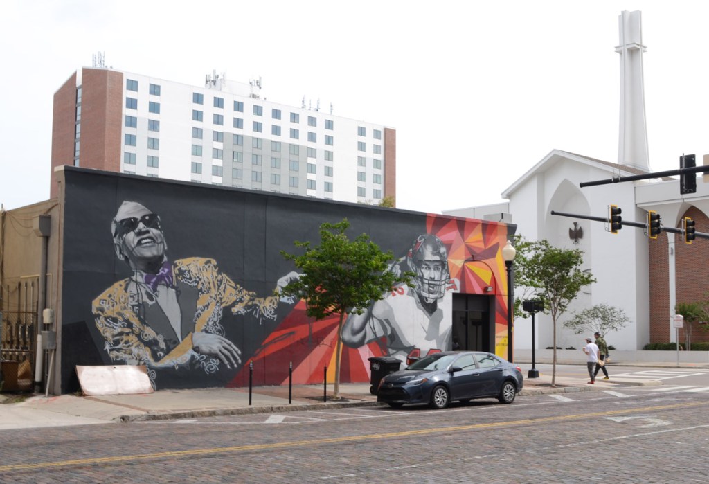 downtown Tampa street with mural by Matt Kress and Audrey Jennifer of Ray Charles in a purple bowtie and quarterback Tom Brady in his Buccaneers uniform, number 12