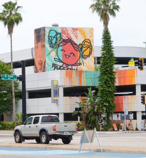 two faces on the top of a parking structure, one is very happy and smiling, the other has a more neutral expression but is a more realistic rendering of a girls face.