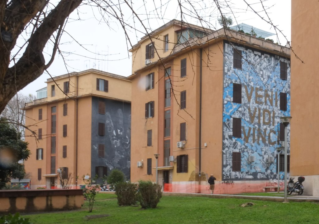 two large murals on the sides of a four storey apartment building in Tor Marancia, Rome, one is a large hand and the other is three words, veni, vidi, Vinci