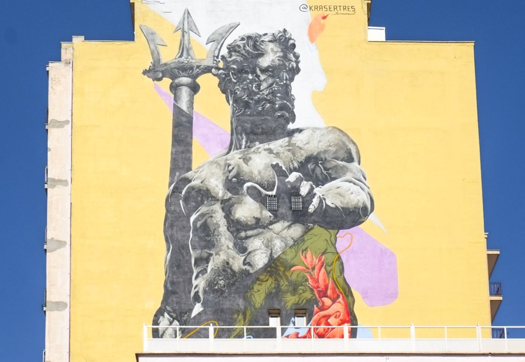 Roman god Neptune, Nettuno, stands holding a trident, seen from the waist up, a mural by Kraser Tres