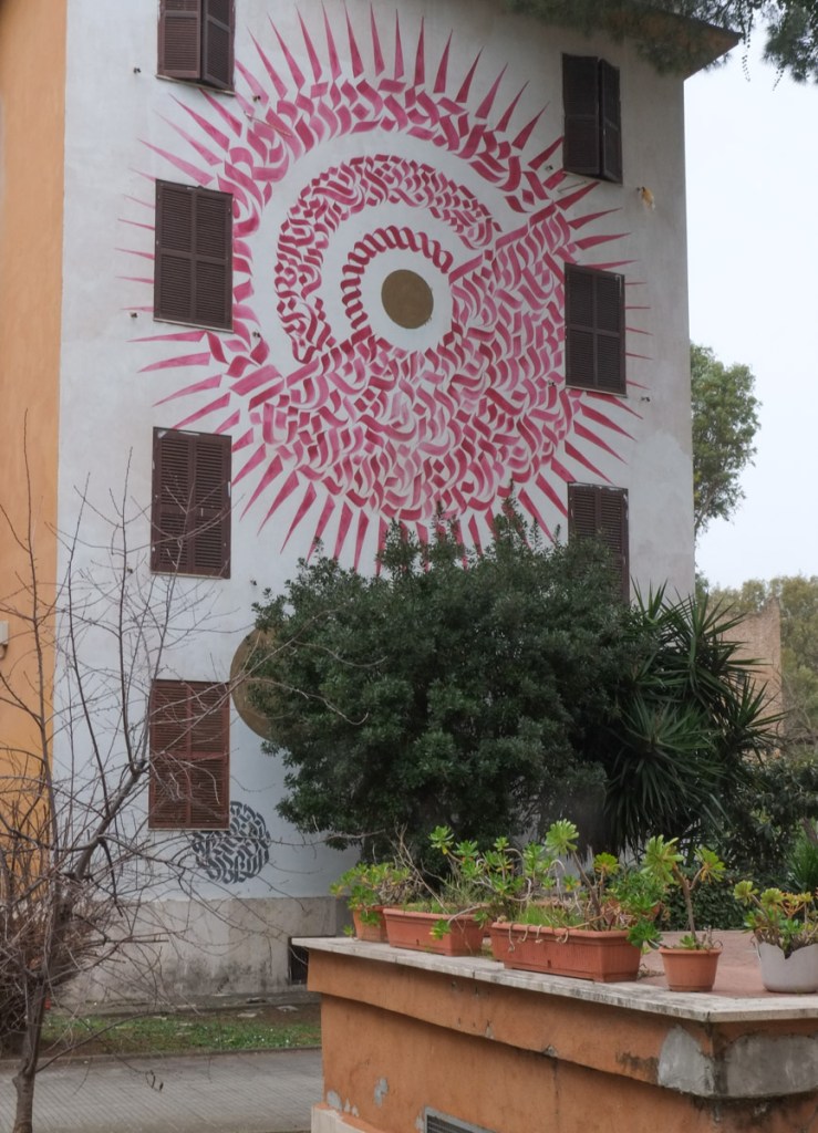 large mural on the side of a four storey apartment building in Tor Marancia, Rome, red on white calligraphy type mural, circle shape, sun-like