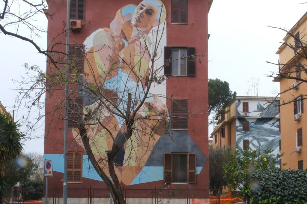 large mural on the side of a four storey apartment building in Tor Marancia, Rome, a man and a woman are hugging, man's face can't be seen, woman is looking out over the street