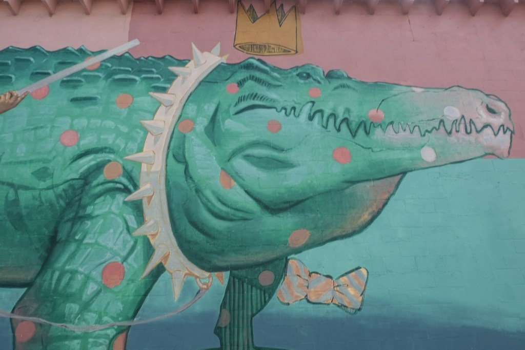large alligator in a mural, greenish blue colour, with gold crown, large spikey collar around its neck