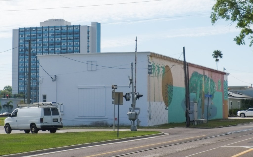 low white building beside street, with mural along the wall, railway tracks, bike trail,