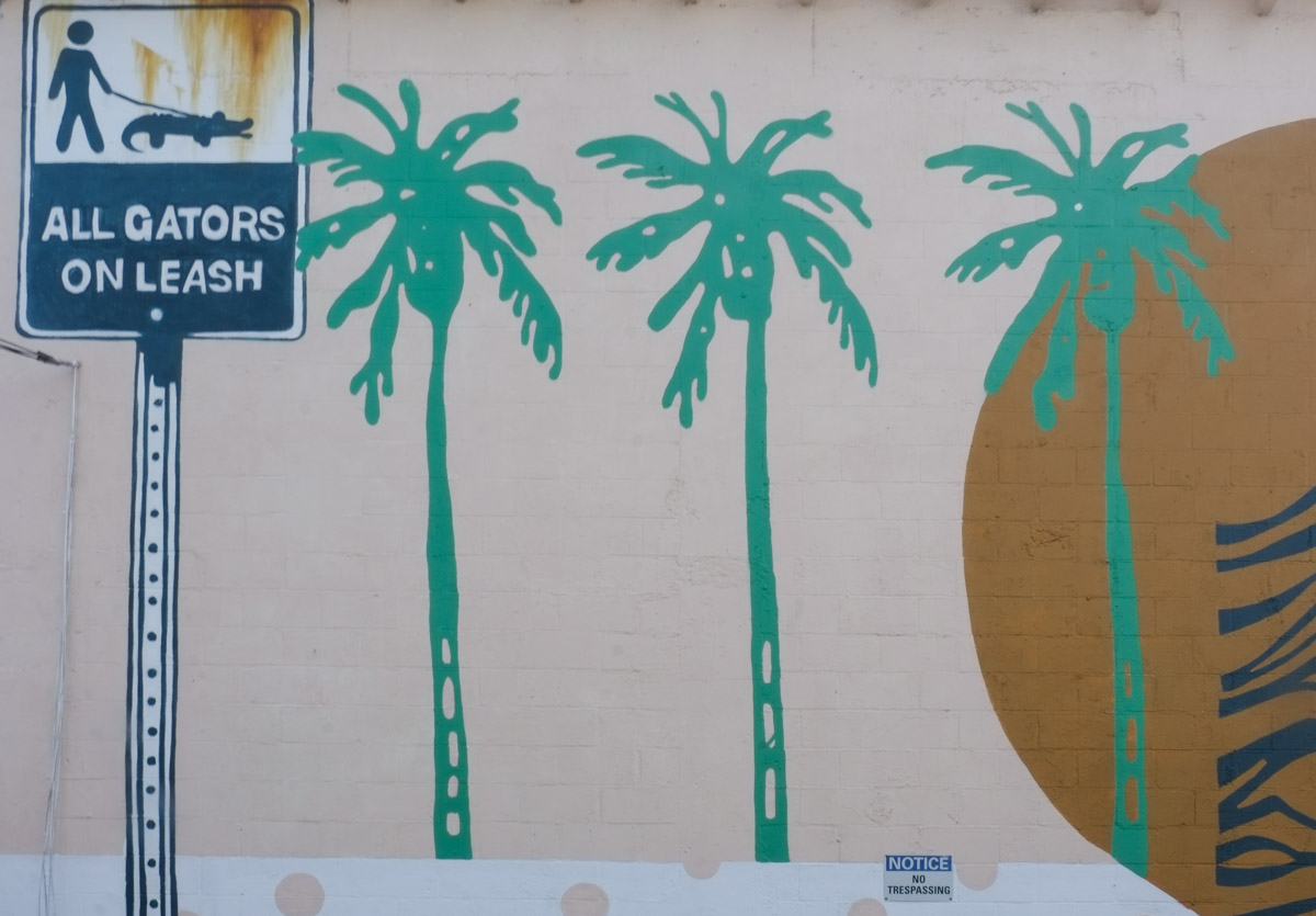 part of a mural, palm trees, a sign that says gators must be leashed