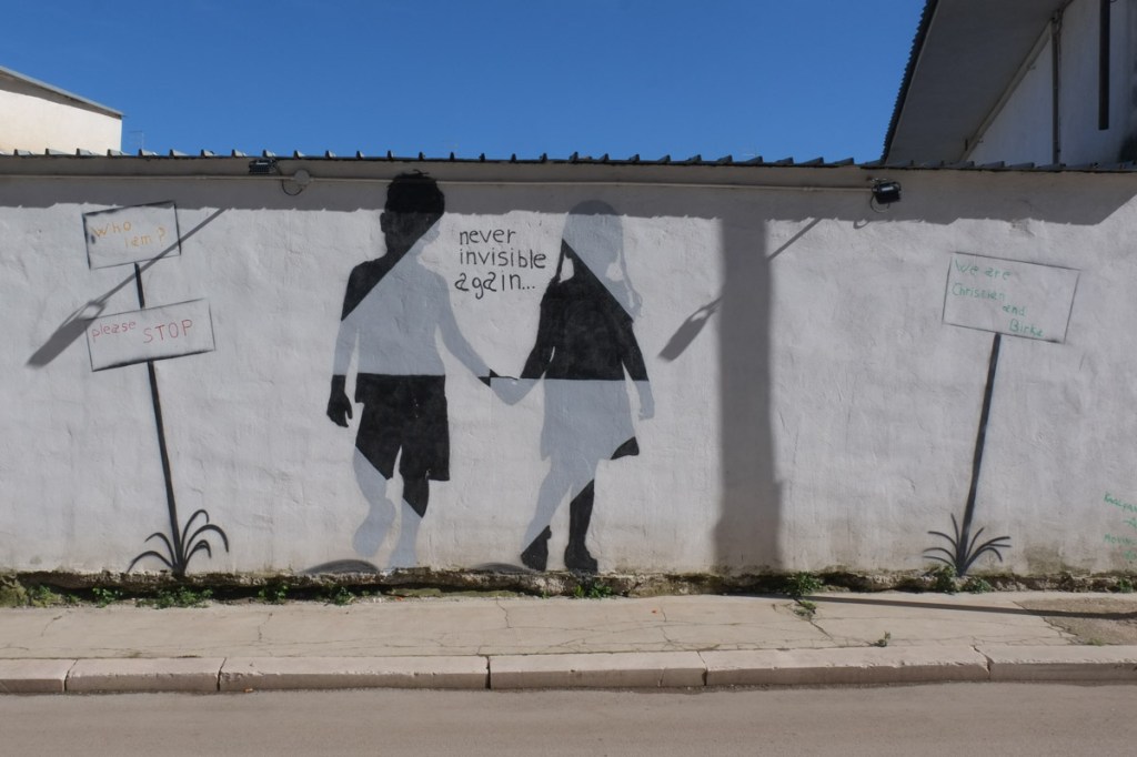two children walking together, back to viewer, image in a mural, along with text that says never invisible again