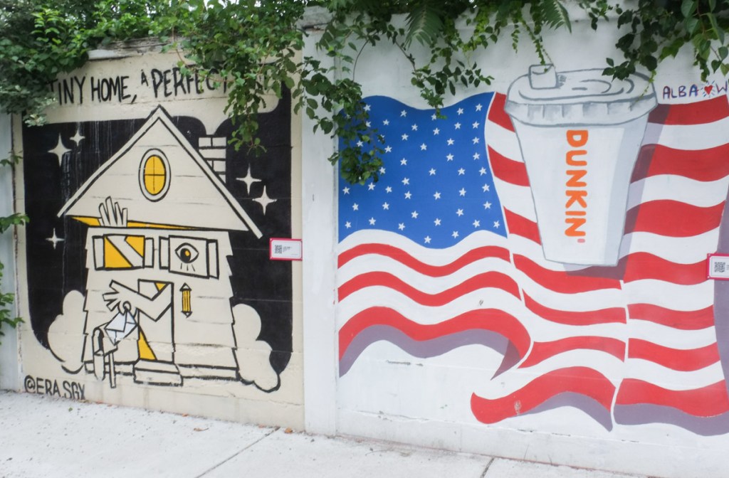 mural on a fence, on the right is a dunkin donuts coffee cup in front of an american flag