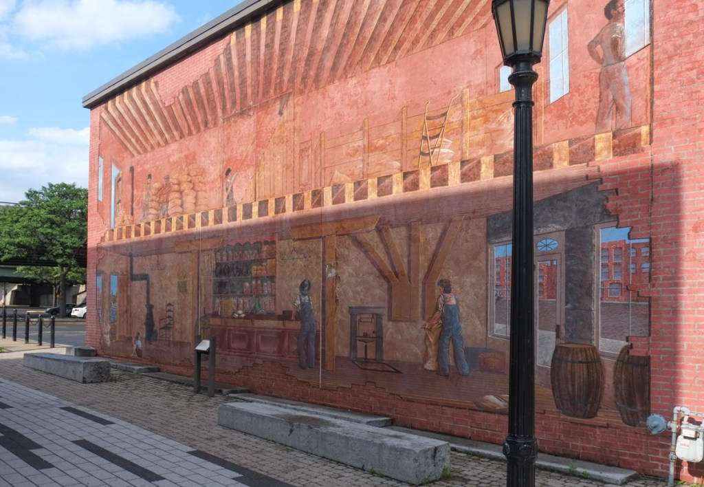 mural on the side of a brick building at the erie canal museum in syracuse new york, scenes from the interior of a warehouse along the canal back in history