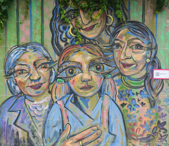portrait of four women standing together, street art on a fence