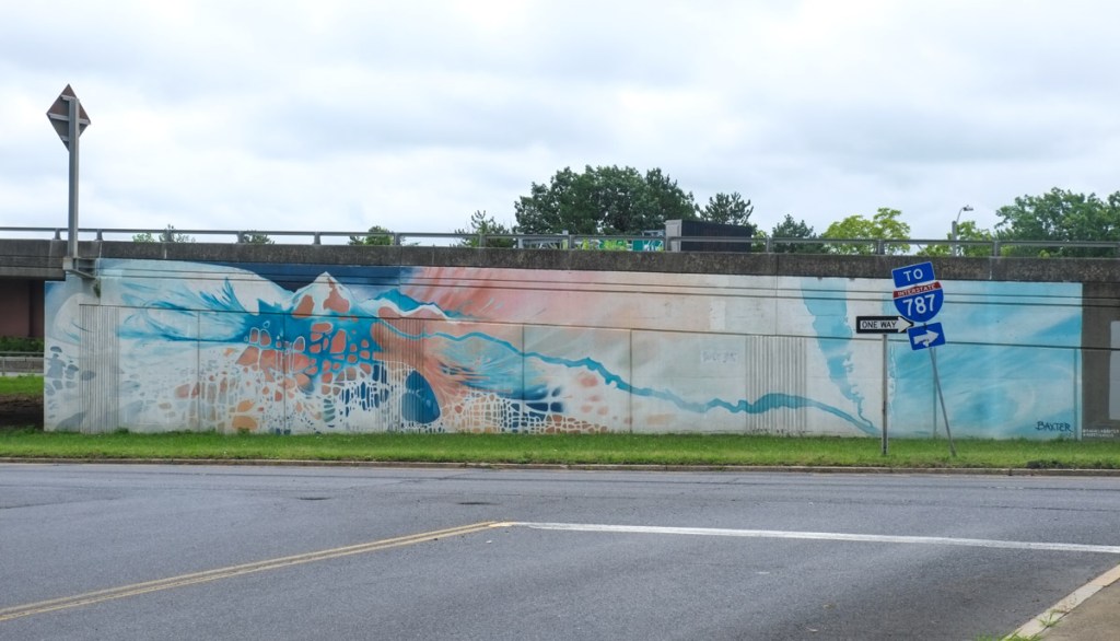 mural on the side of an elevated section of freeway in albany by rachel becker, orange and blue on white