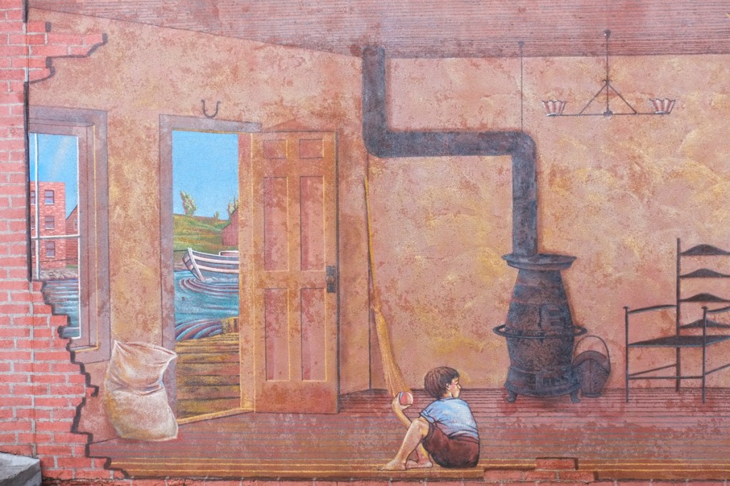 part of a mural, boy sitting on floor, open door and window with views of boat on canal outside, a black pot bellied stove in the room too
