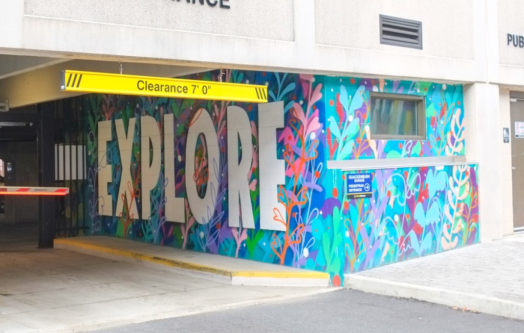 mural on the side of an entrance to a parking garage, with large text says explore