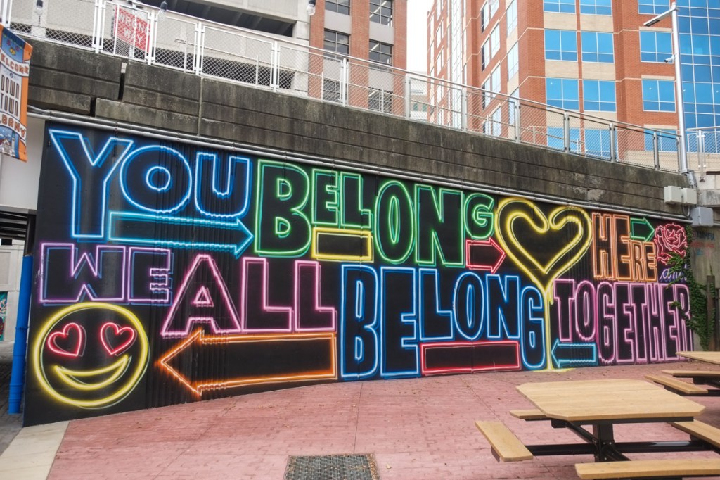 mural with words, you belong here we all belong together, each word in a different colour, along with a happy face with heart shaped eyes, and a large yellow heart