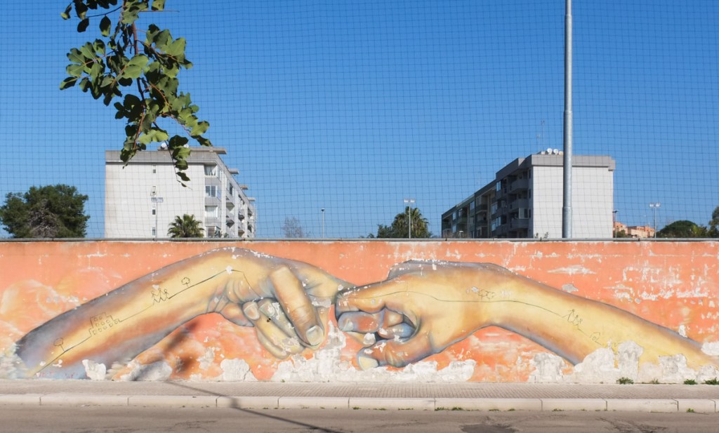 long horizontal mural on a fence, to arms and hands coming together in the center to link fingers