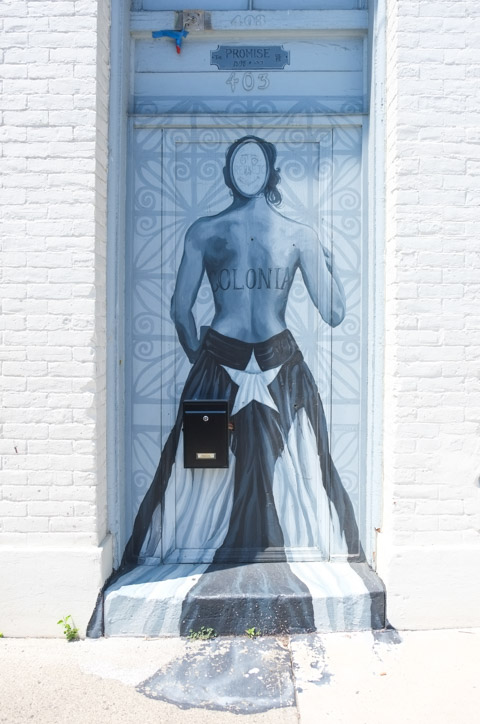 painting on a door at number 403, back of figure with word colonia written across the back, smiley face graffiti on the head, 