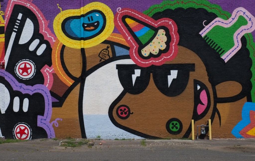 close up of part of mural by Golden 305 in Holyoke Massachusetts, brown unicorn with white t shirt and ice cream cone as horn, green comb in his curly black hair , wearing converse all star running shoes