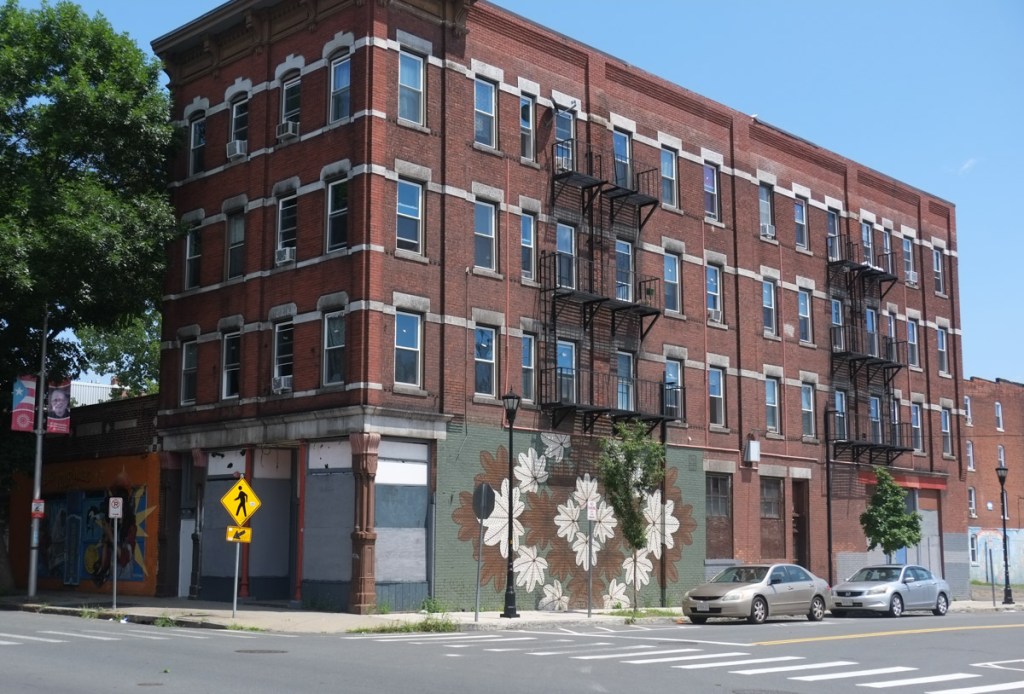 mural on an old brick building, by vero rivera, design using patterns of brown and white leaves
