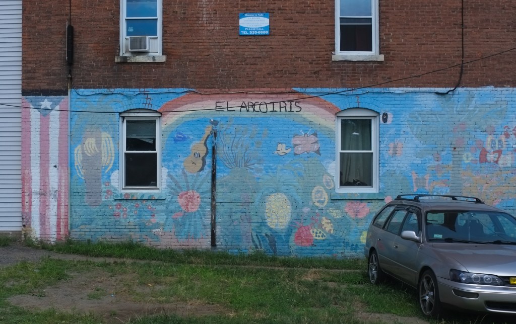older faded el arcoiris mural with flowers, butterflies, rainbow and a Puerto Rican flag