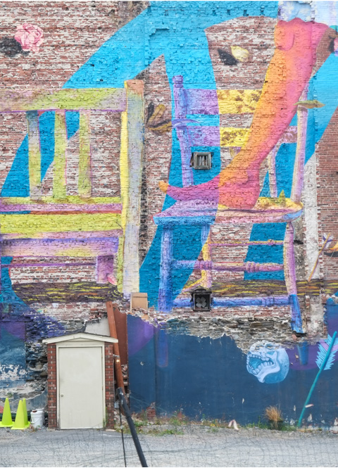 large mural by David Zayas, girl in skirt and bare feet walks over a row of chairs, from seat to seat 