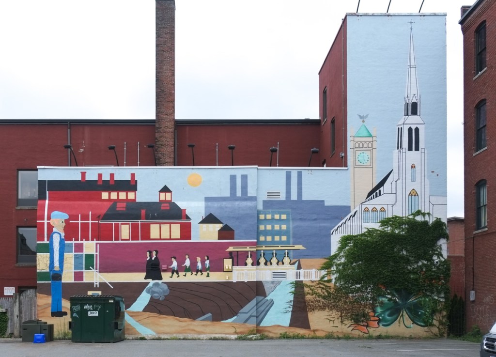 Large mural in Lowell, on the side of old factory building, historic iage of old factory with people going to work, also two large churches in the mural, Irish heritage of the area, 
